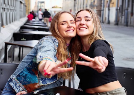 Two cheerful teenage friends enjoying time together outdoors, smiling and posing with peace signs.