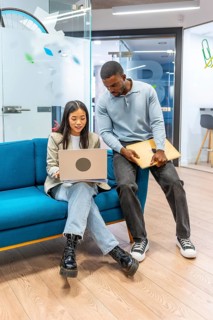 Two young professionals working together, sharing ideas and using a laptop in a modern coworking