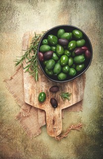 Chalkidiki olives, classic Greek green olives, in a bowl on a cutting board, top view, without