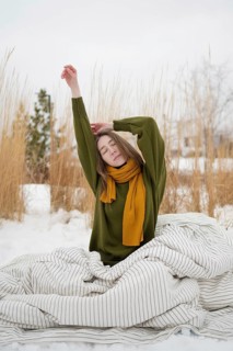 A woman with a serene expression stretches in a snowy park, wearing a green sweater and yellow