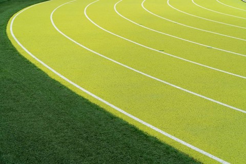 Overhead view of vibrant green lanes vividly marking the curves on an outdoor athletics stadium,
