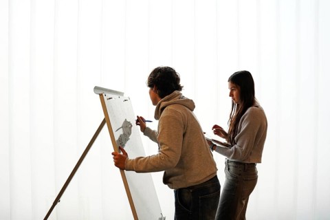 Two teenagers, a non-binary individual and a female, participate in an writing activity, o a