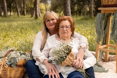 An affectionate mother and daughter pair sit in an idyllic grassy field, surrounded by nature's