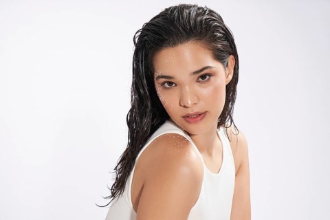 A striking female model with wet hair looks at the camera, showcasing a natural beauty look in a