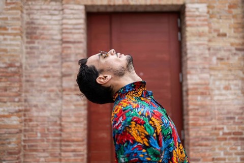 A fashionable cuban man wearing a colorful tropical shirt leans back with his head tilted and
