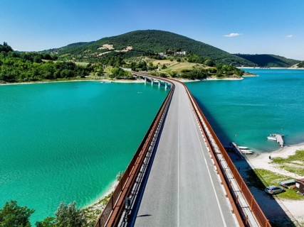 A breathtaking view of a bridge extending over a turquoise lake surrounded by lush hills in Italy,