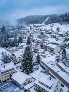 Aerial view of a snow-covered village surrounded by forests and mountains in winter, Enzklösterle,