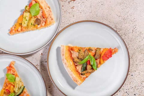 Delicious vegetarian pizza slices topped with vibrant zucchini, eggplant, olives, and basil. Served