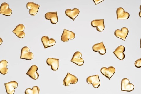 Numerous golden heart shapes artistically arranged on a plain white surface, symbolizing love and