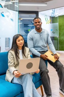 Two smiling business people holding a laptop and a tablet in a modern coworking office, showcasing