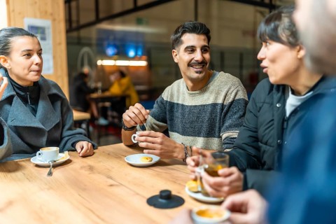 Diverse group of friends socializes and talks while drinking coffee and tea at a wooden table in an