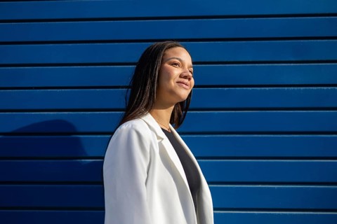A confident businesswoman in a white blazer smiles against a vibrant blue background. Her