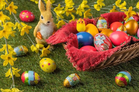 A basket full of colorful Easter eggs and a rabbit figurine with yellow flowers and chocolate eggs