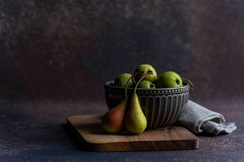 A rustic display of fresh wild pears in a textured ceramic bowl sitting atop a wooden surface