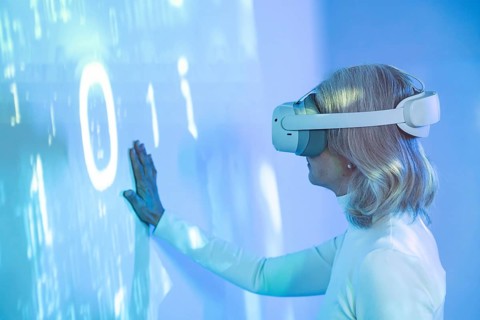 An elderly Asian woman interacts with the virtual world wearing a VR headset, symbolizing the