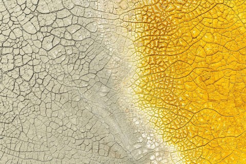 A close-up of cracked mud with striking multicolor patterns, featuring vivid yellow on one side and