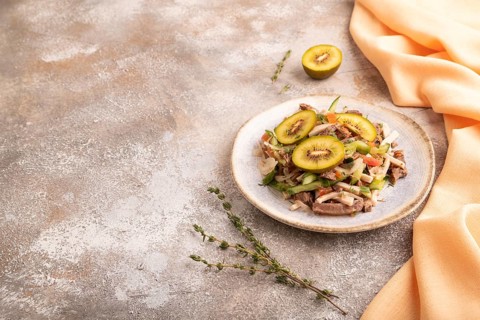 Meat salad with beef kiwi and vegetables on brown concrete background and orange linen textile.
