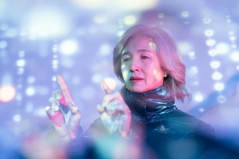 An elderly Asian woman explores the metaverse, engaging with virtual holographic displays. The