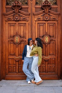 A lesbian couple smiling and embracing in front of an ornate wooden door, exuding love and