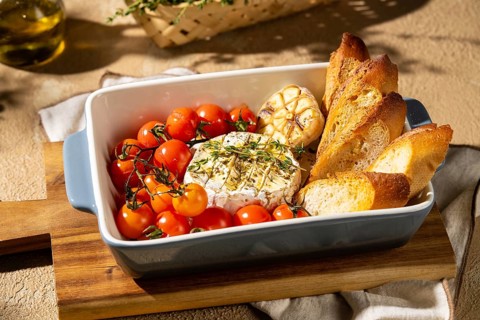 A savory dish featuring baked Camembert cheese garnished with herbs, surrounded by roasted cherry