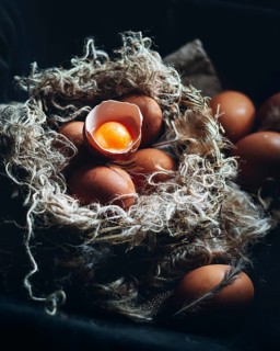 Close-up image of farm-fresh brown eggs nestled in a rustic, straw-lined nest. One egg is cracked