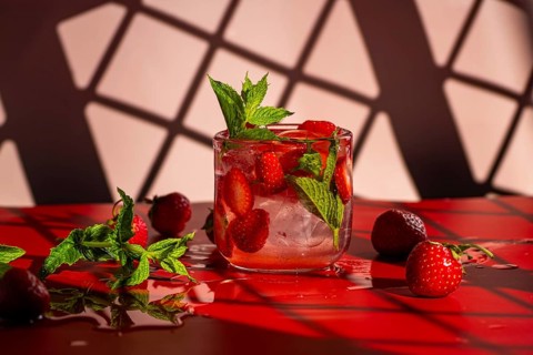 A vibrant strawberry mojito cocktail garnished with fresh mint leaves sits on a glossy red surface.