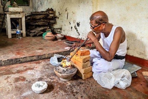An old man works with fire and bricks in a workshop, he looks concentrated, a man burns sapphires