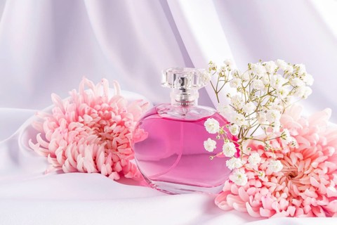 A stylish perfume bottle filled with pink liquid is elegantly nestled among pink flowers and white