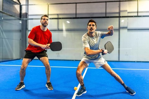Two active men engaging in a pickleball match on a blue indoor court, concentrating on hitting the