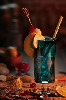 Cocktail in a glass with ice cube cubes, decorated with lime slices and cherries on a sandy