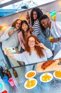 Vertical photo of a group of multi-ethnic friends gesturing success while taking selfie during
