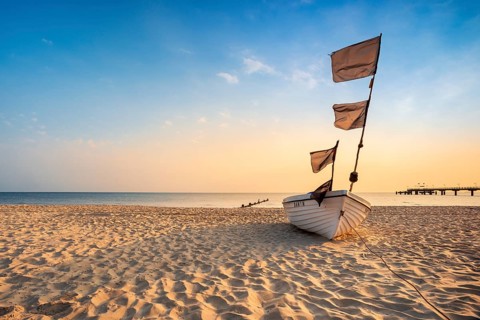 Fishing boat with black flags on a fine sandy beach in the morning light, Baltic resort Bansin,