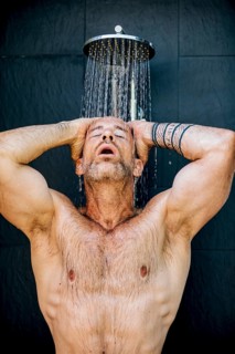 A man stands under a rainfall shower head, enjoying the refreshing flow of water. With closed eyes