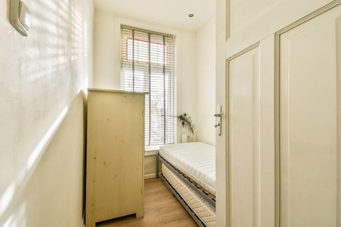 A bright and cozy room featuring a wooden cupboard and a neatly made bed, complemented by natural