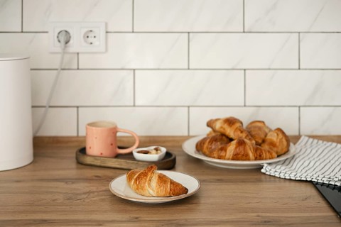 Delicious homemade croissants arranged on a rustic wooden table, captured alongside a warm cup of