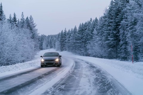 A car drives along a snow-covered road, flanked by dense, snow-laden trees in the serene Swedish