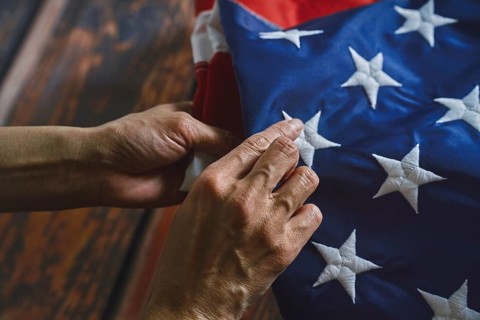 Close-up of hands reverently folding an American flag, emphasizing intricate stitching and vibrant
