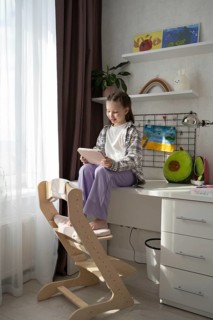 A child sits on a desk, engaged with a tablet, surrounded by vibrant art, plush toys, and