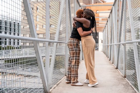 A loving LGBT multiethnic couple embraces on a metal bridge in an urban setting. Their warm hug