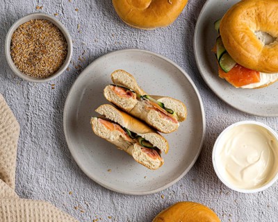 A top view of bagels with salmon and cream cheese on a speckled plate. A bowl of cream cheese and a