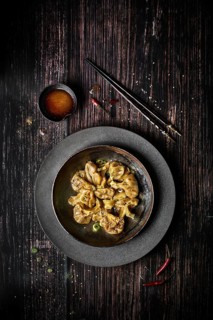 View from above of a plate of chili wontons on a wooden table next to chopsticks