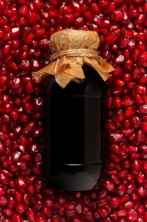 Pomegranate sauce in a bottle, top view, in pomegranate seeds, food background, vertical, no people