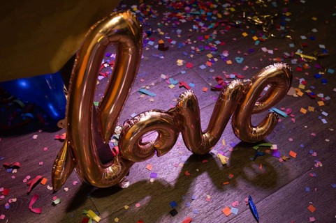 A golden foil balloon spelling love on a wooden floor covered in colorful confetti, creating a