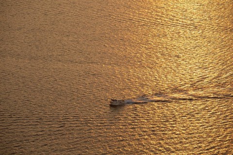 A small boat glides through the shimmering golden waters of the Mediterranean Sea at sunrise,
