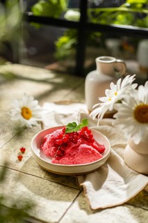 From above a homemade pink berry mousse topped with fresh red currants and green leaves, elegantly