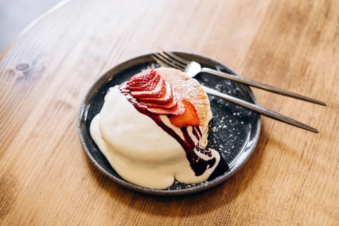 Fluffy japanese pancakes topped with fresh strawberries, a drizzle of cream, and berry sauce.