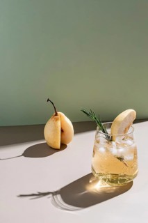 A refreshing summer cocktail adorned with a slice of pear and rosemary sprig, set against a
