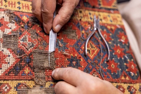 Close-up of a cropped unrecognizable senior male artisan's hands precisely restoring a colorful,