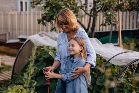 A joyful mother daughter duo tends to their greenhouse, surrounded by lush plants. They share a