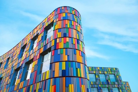 Low angle of a vibrant multicolor facade adorns a modern curved building, presenting a striking